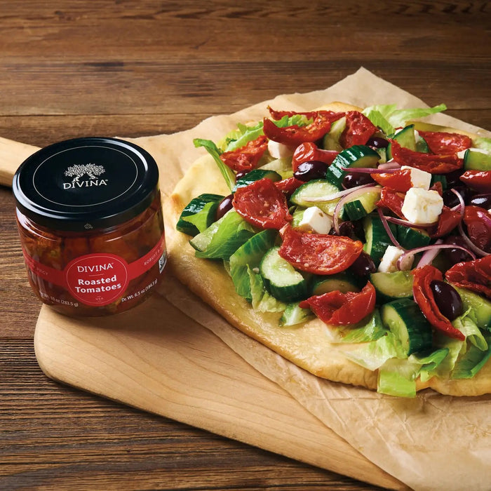 A glass jar of DIVINA Roasted Tomatoes with a black lid displays the marinated, USA-grown tomatoes inside. The label is red with white text, and the net weight is 10 oz (283.5 g).