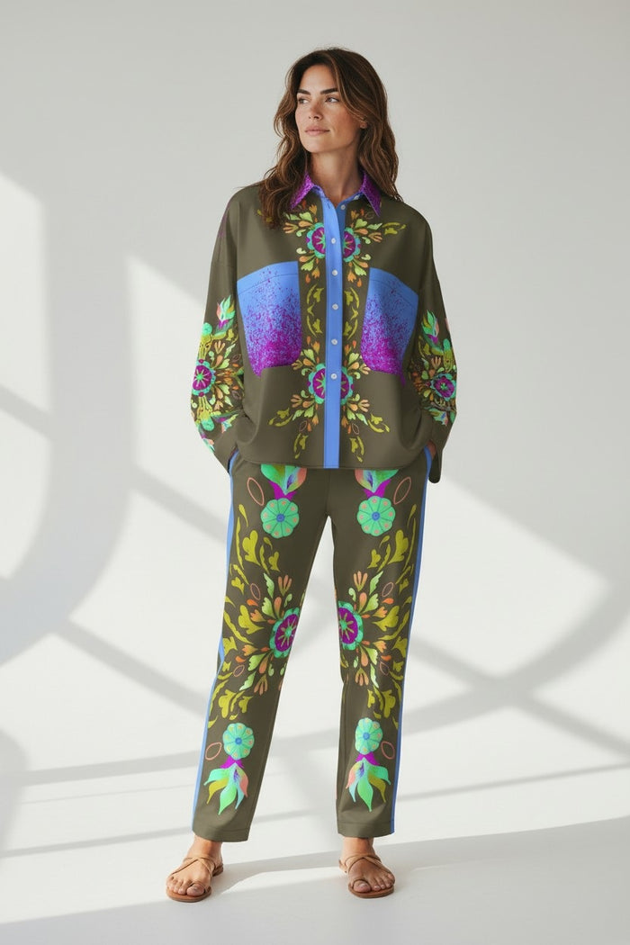 A woman with wavy brown hair wears the FRANCO FERRARI Silk Blouse, featuring colorful blue, purple, and green floral patterns and large front pockets, standing against a light background and smiling slightly to the side.