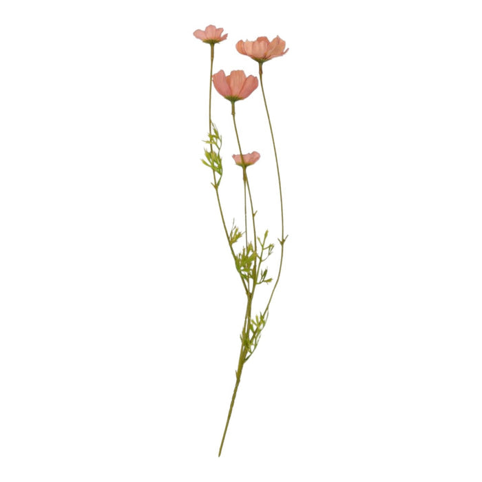 The ABIGAIL AHERN SOFT PINK COSMOS MEADOW arrangement in a textured glass vase sits on a light wood table beside beige and brown tea light holders, creating a soft botanical vibe. A blurred dark chair appears in the background.