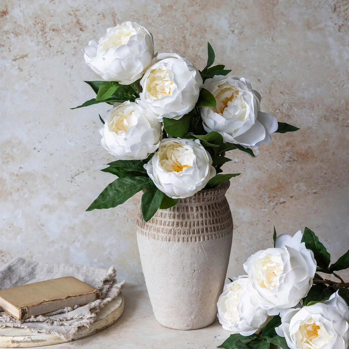 The ABIGAIL AHERN - WHITE PEONY features five real-touch white peonies with green leaves in a textured beige vase, styled against a light neutral background, reflecting ABIGAIL AHERN’s signature aesthetic.