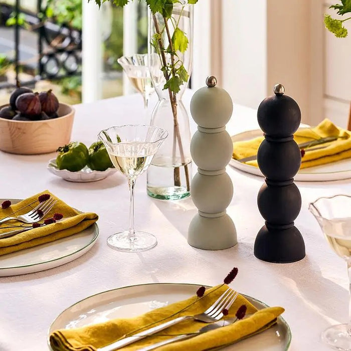 A green shelving unit displays a striped vase with white flowers, ADDISON ROSS SCANDI BOBBIN salt or pepper mill, a black and white patterned bowl, and a framed Campari Soda poster with a red bottle.