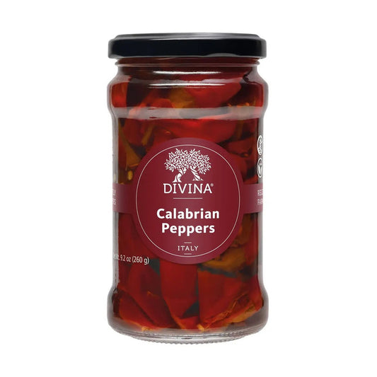 A blue bowl filled with vibrant red DIVINA - CALABRIAN PEPPERS, their stems still attached, sits on a beige cloth with dark stripes atop a wooden surface.
