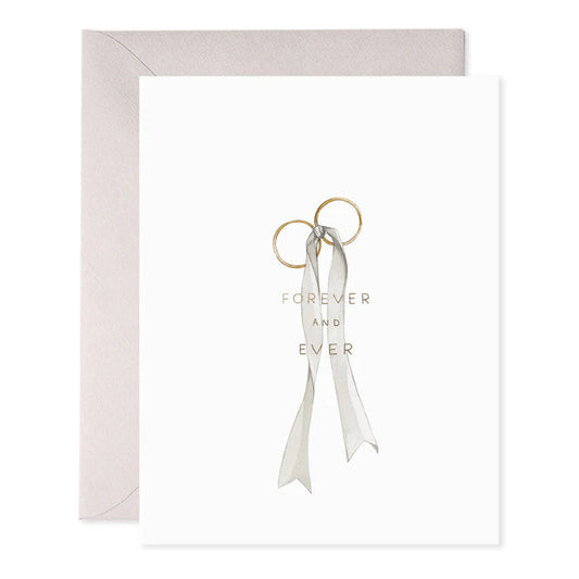 The E. FRANCES PAPER Wedding Rings Greeting Card showcases two intertwined gold rings tied with a gray ribbon and elegant foil accents, inscribed with "FOREVER AND EVER." A handcrafted watercolor touch enhances the card, complemented by a beige envelope.