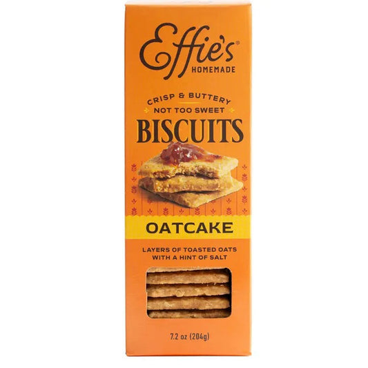 Two glass bowls filled with yogurt, blueberries, peach slices, and crumbled EFFIES - ORIGINAL OATCAKE BISCUIT by EFFIES HOMEMADE. A box of Effies Homemade Oatcake Biscuits, whole biscuits displaying their buttery layers, and golden spoons sit alongside. In the background, there’s a plate with peach slices.