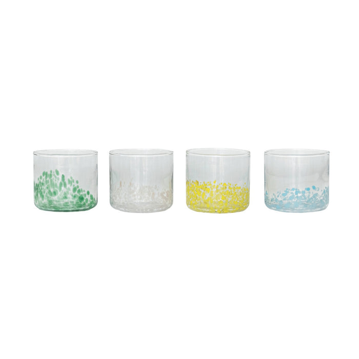 A round tray displays two CREATIVE COOP HAND-BLOWN ROUND CONFETTI DRINKING GLASSES with beverages, decorative stirrers, a green bottle, lemonade bottle, and a small cactus ornament on a tabletop with light linens.