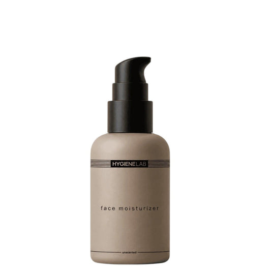 A bottle of HYGIENELAB - FACE MOISTURIZER, UNSCENTED from HYGIENELAB rests on a dark slate surface, surrounded by smooth black stones and a smear of white cream accented with a dark streak—an unscented men’s face moisturizer formulated with ceramides to promote healthy, hydrated skin.