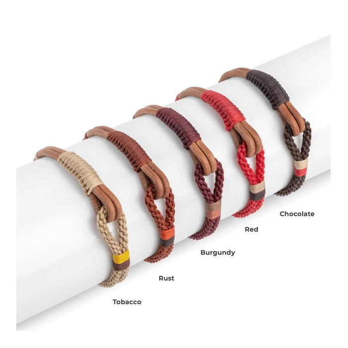 A close-up of a person's wrist wearing the MAKARLA MEN'S NAUTICAL ROPE BRACELET IN CHOCOLATE, featuring braided rope and a wooden clasp, set against a white fabric background.