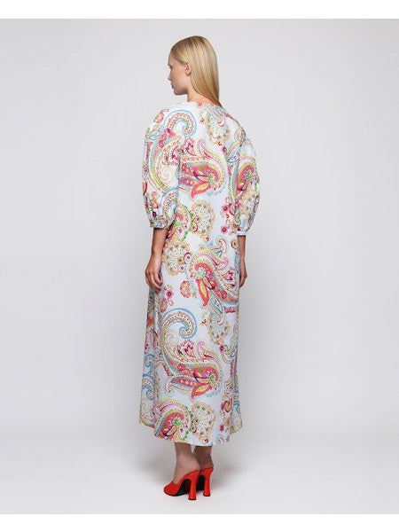 A woman faces forward in the MIRTO 1956 Paisley Print Long Sleeve Dress, featuring multicolor linen, puffed three-quarter sleeves, and a V neckline. She has straight blonde hair, red shoes, and stands against a plain white background.