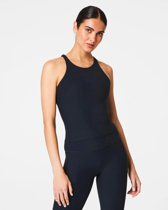 A woman with dark hair tied back wears the SPANX ONFORM High Neck Tank in Black, standing against a plain white background and looking at the camera.