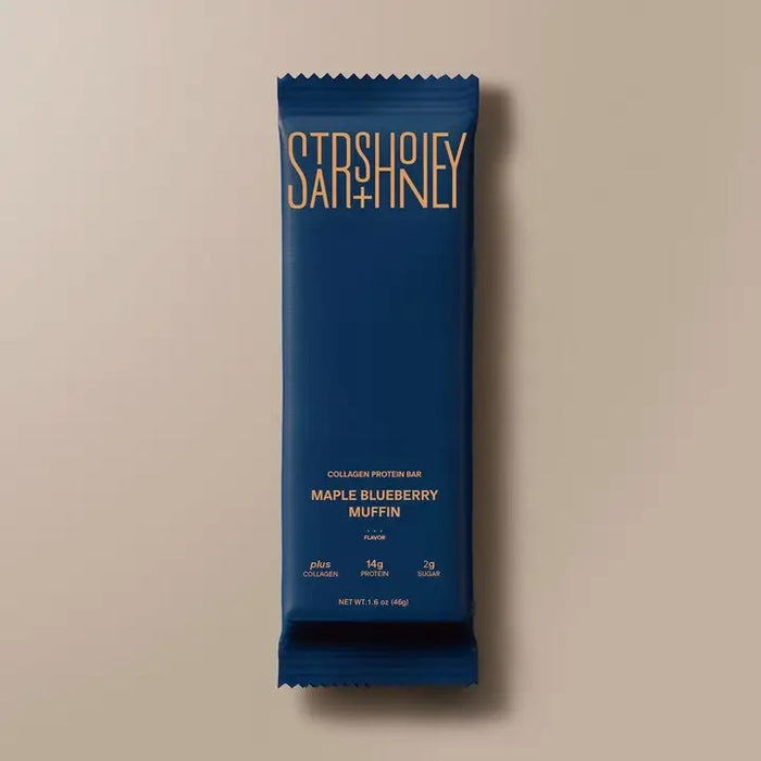 A blue wrapper labeled “STARS+HONEY - MAPLE BLUEBERRY MUFFIN”—a tasty collagen protein bar blending maple and blueberry flavors from the brand STARS+HONEY—rests on a beige surface, with nutritional information visible.