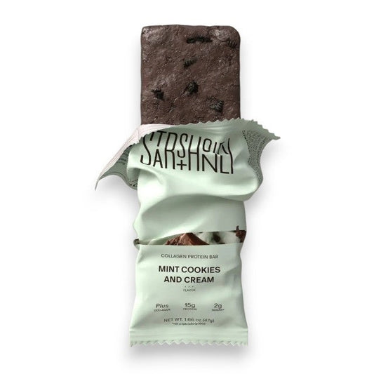 A STARS+HONEY - MINT COOKIES & CREAM Collagen Protein Bar, with its wrapper, displays mint chocolate ice cream and cookie pieces bursting out for a dynamic effect against a beige background.
