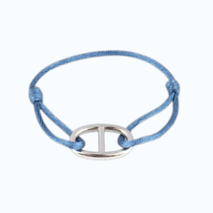 A close-up of a wrist wearing the STOLEN RICHES Viseu String Bracelet with Anchor Chain Fixture in light blue, paired with a light blue shirt and dark pants, highlights this nautical accessory from STOLEN RICHES.