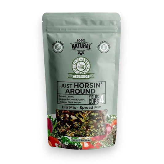 A package of TO MARKET - JUST HORSIN’ AROUND DIP MIX from TO MARKET- DIPS & SPREADS is displayed behind a white bowl of dip accompanied by two crackers. The package highlights zesty ingredients such as horseradish, garlic, and sun-dried tomatoes, and notes that it’s salt-free, gluten-free, and makes 4 cups.