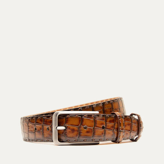 The WILL LEATHER GOODS - CROCO BELT IN COGNAC features Italian leather with a crocodile pattern and a silver buckle, shown coiled loosely on a light background.